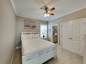 A bedroom with a bed, a ceiling fan, a painting, a window with blinds, and a door.