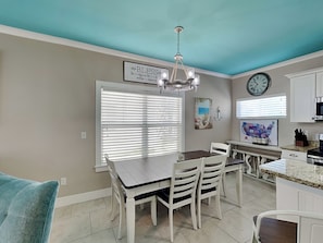 A kitchen with a dining table, chairs, a chandelier, a clock, and a map on the wall.