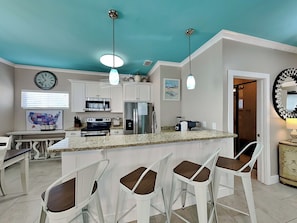 A kitchen with a central island, bar stools, a clock, and a refrigerator.