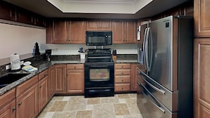 Una cocina moderna con armarios de madera, un refrigerador de acero inoxidable, un horno negro y un microondas.