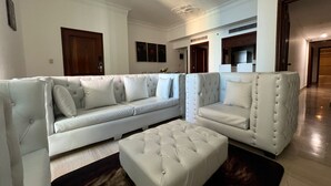 A modern living room with a large L-shaped sectional sofa, a matching ottoman, and a dark wood floor. - Exclusive 3 BDR, Gym & Pool, Sea view Condo (Santo Domingo)