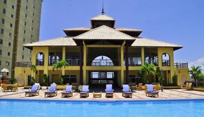 A hotel with a pool area, multiple lounge chairs, and a large building with a tiled roof. - Exclusive 3 BDR, Gym & Pool, Sea view Condo (Santo Domingo)