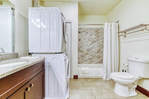 A bathroom with a marble shower, a white toilet, and a washing machine.