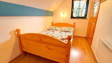 A small bedroom with a wooden bed, a window with curtains, and a wall-mounted light.
