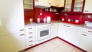 A kitchen with white cabinets, red accents, a built-in oven, and a tiled backsplash. - Apartment Sara (Vitanje)