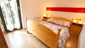 A bedroom with a wooden bed, two bedside tables with lamps, a red accent wall, and a view through a glass door. - Apartment Sara (Vitanje)
