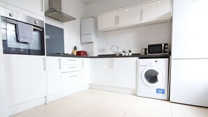 A modern kitchen with white cabinets, a built-in oven, a microwave, and a washing machine. - Spacious 2 Bedroom Duplex (Reading, Berkshire)