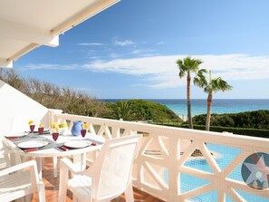 A balcony with a table set for dining, overlooking a pool and the sea. - Apartment 5 In front of the sea (Urbanització Santo Tomàs, Es Migjorn Gran)
