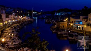 A marina at night with boats docked, buildings along the waterfront, and street lighting.