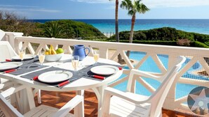 A dining table set with plates, cutlery, and glasses, overlooking a pool and a scenic ocean view.