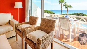 A balcony with wicker chairs, a white table, and a view of the ocean.