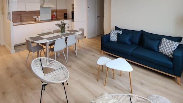 Un salón moderno con un sofá azul oscuro, sillas blancas y una mesa de comedor.