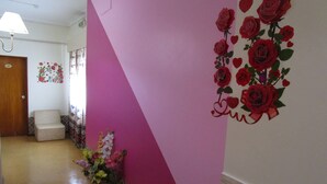 A hallway with a pink wall, a wooden door, a white wall with a floral decoration, and a potted plant. - Residencial Pimenta (Portimão)