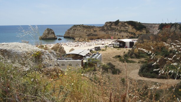 A coastal area with a rocky landscape, a beach, and several white buildings with flat roofs, likely part of a resort or hotel. - Residencial Pimenta (Portimão)