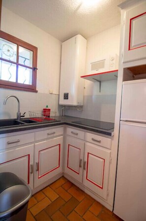 A compact kitchen with white cabinets, a black countertop, a sink, and a window with a wooden frame. - Nice Apt of 35m²  at 450m from the beach (Saint-Raphaël)