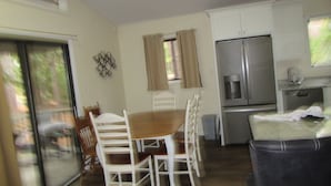 Een kleine keuken met een eettafel, stoelen, een koelkast en een schuifpui.