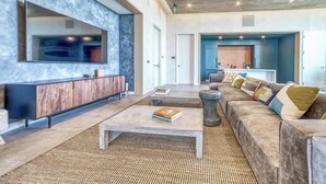 A modern living room with a large flat-screen TV, a wooden cabinet, a sofa with cushions, and a coffee table. - Frisco - Rooftop pool & gym on Rainey St (Austin)