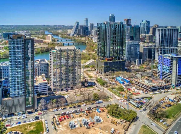 A cityscape with modern high-rise buildings, a river, and a construction site. - Amarillo - Rooftop pool on Rainey St (Austin)