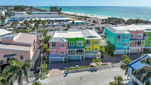 A colorful beachfront hotel with multiple buildings, a parking lot, and a beach in the background.