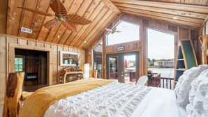 Une chambre de style cabane en bois, avec un grand lit, un ventilateur de plafond et une vue sur l’extérieur.