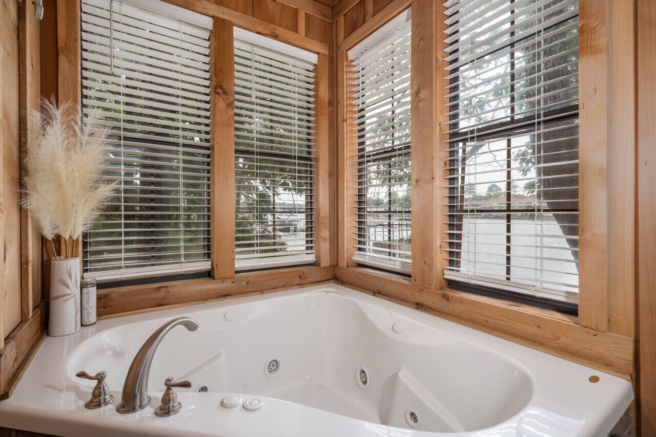 Una cabaña de madera con una bañera grande, marcos de ventanas de madera y un florero con plumas de pampa.