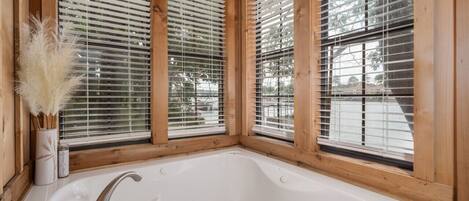 Una cabaña de madera con una bañera grande, marcos de ventanas de madera y un florero con plumas de pampa.