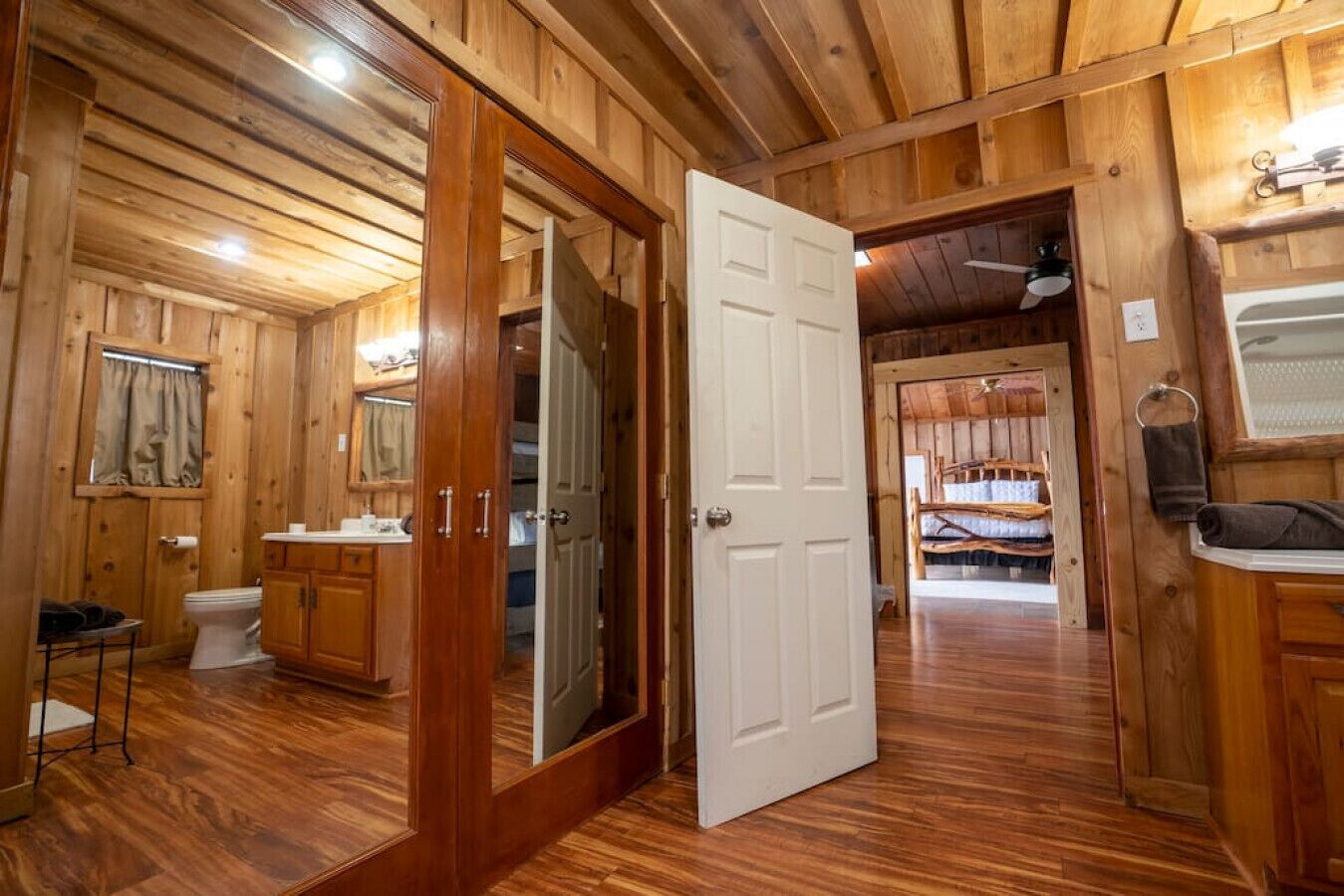 A wooden cabin interior with a bathroom, a bedroom with a bed, and a dining area.