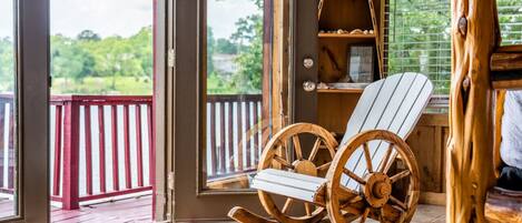 A wooden rocking chair in a room with a large window, a wooden shelf, and a view of a red railing outside.