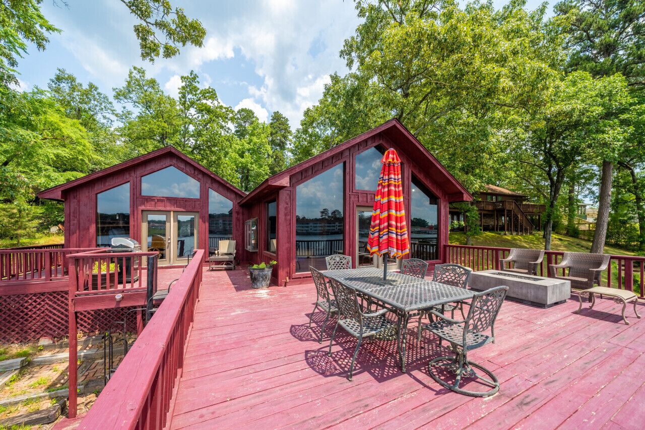 A wooden deck with a dining table and chairs, surrounded by glass windows and a red umbrella.