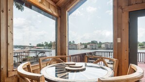 Une terrasse en bois avec une table ronde et des chaises, d’où l’on a vue sur une étendue d’eau et des bâtiments.