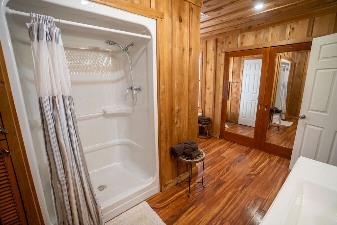Un baño de cabaña de madera con una bañera, una ducha y un taburete pequeño con una toalla.