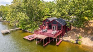 Une cabane rouge dotée d’une terrasse qui surplombe une étendue d’eau, entourée d’une forêt dense.