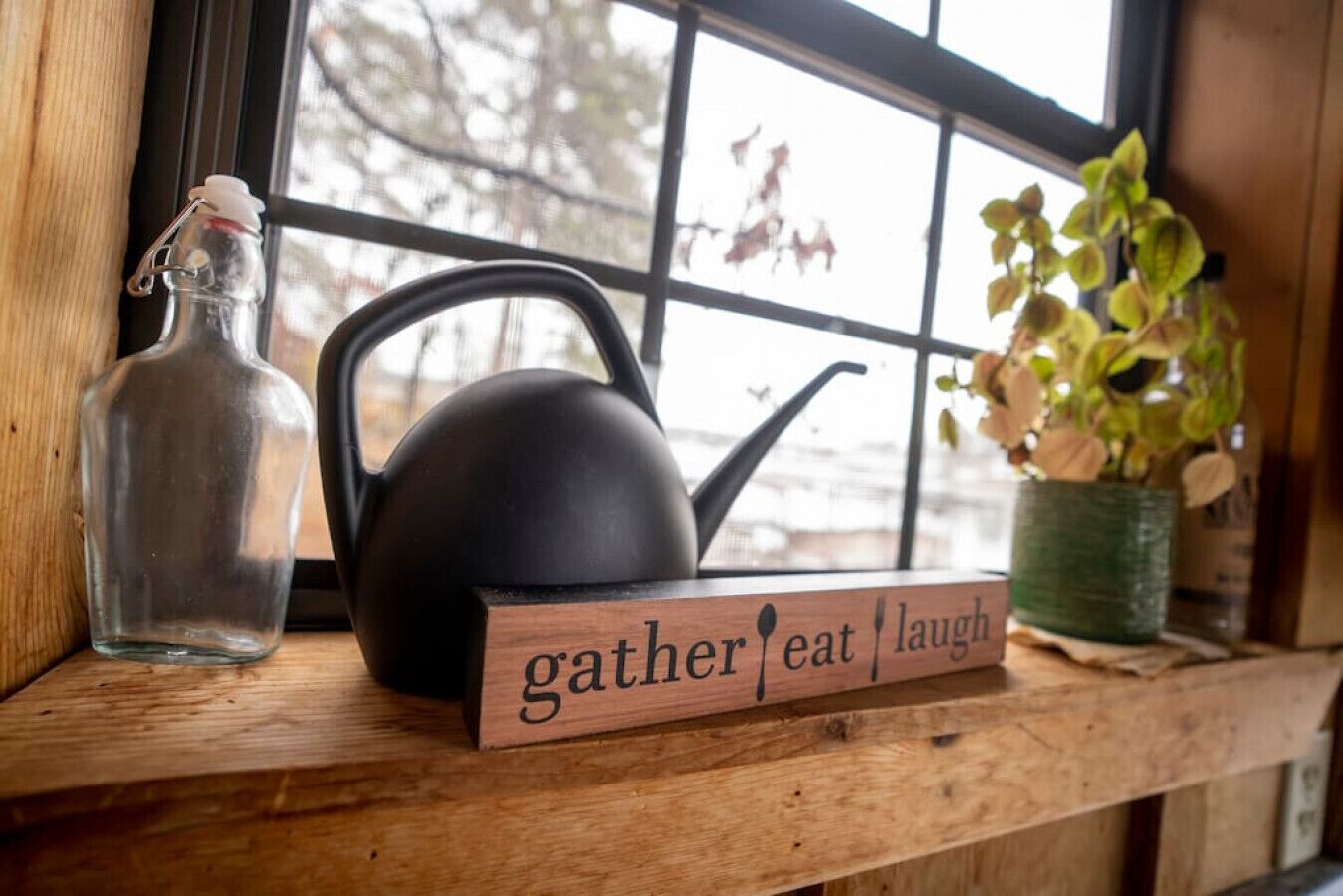 A wooden shelf with a black kettle, a clear glass bottle, and a potted plant.