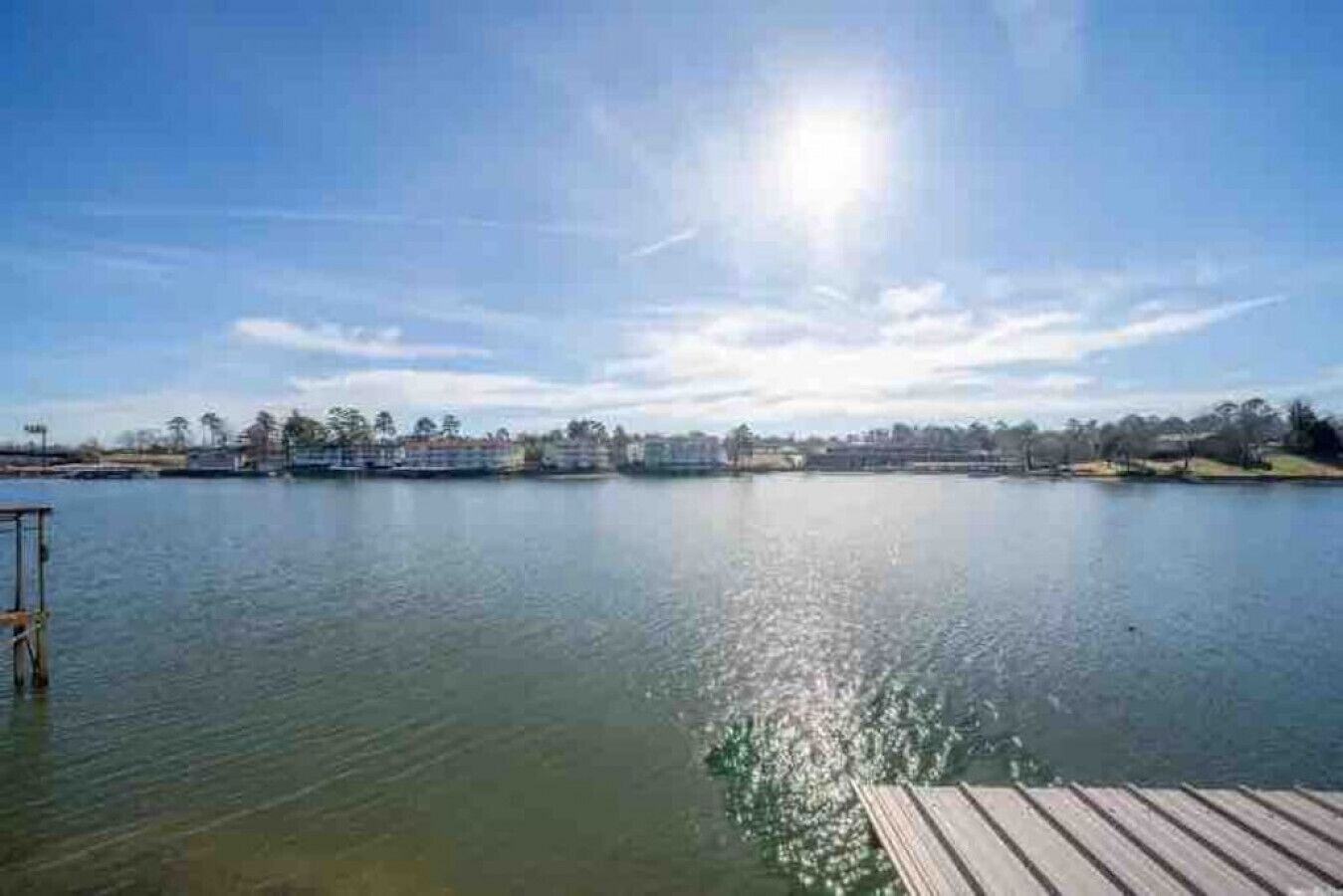 A calm lake with a wooden dock, buildings in the background, and a clear sky.