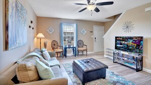 Ein Wohnzimmer mit Sofa, Hocker, TV-Möbel, Deckenventilator und Kunstwerken.