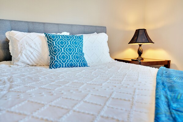 A neatly made bed with a patterned blanket, a blue and white pillow, and a bedside lamp on a wooden nightstand.