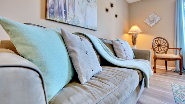 Ein Wohnzimmer mit einem beigefarbenen Sofa, mehreren Kissen, einem dekorativen Sessel, einem Wandbild und einer Lampe.