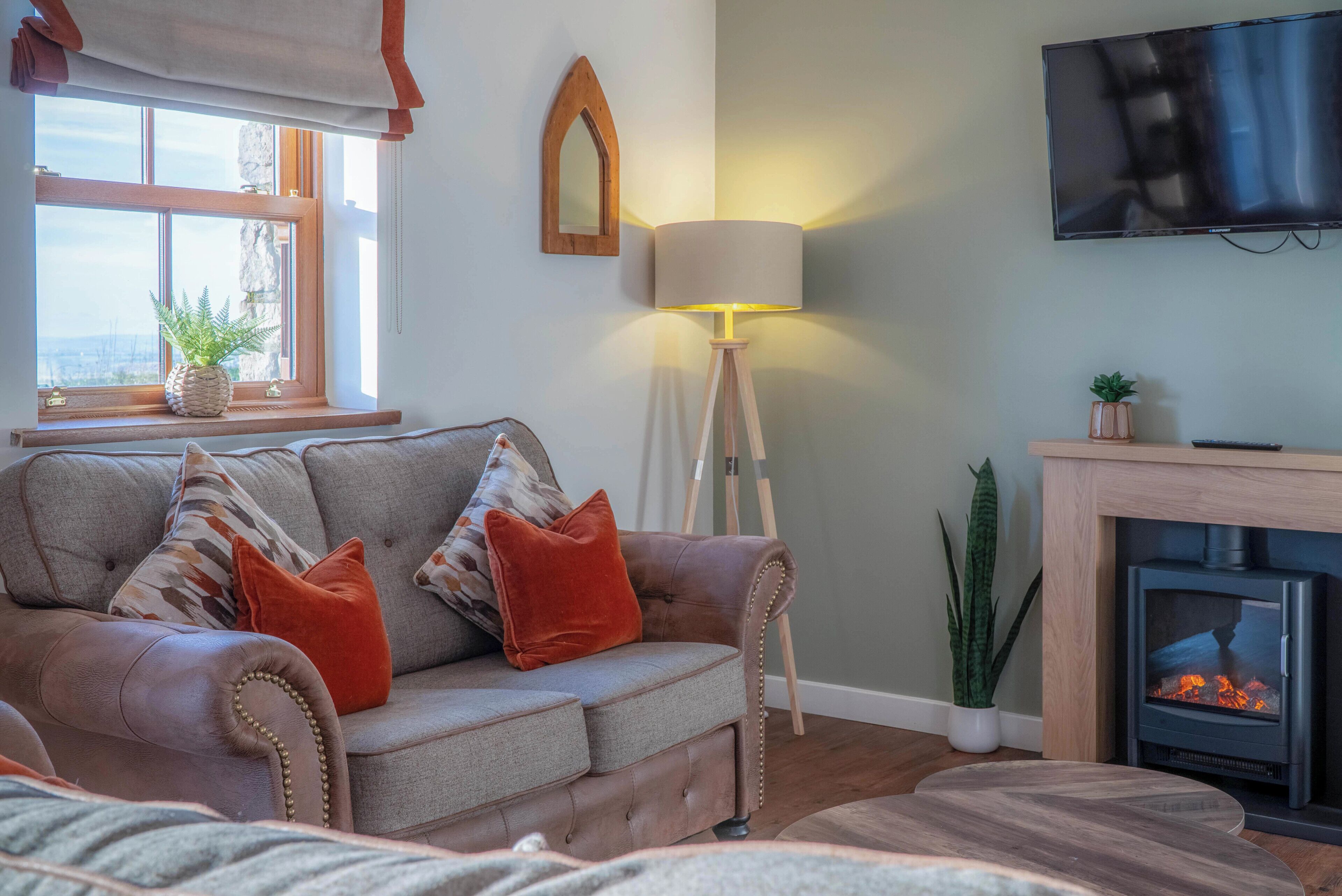 Ein gemütliches Wohnzimmer mit einer Couch, einer Lampe, einem Kamin und einem an der Wand befestigten Fernseher.