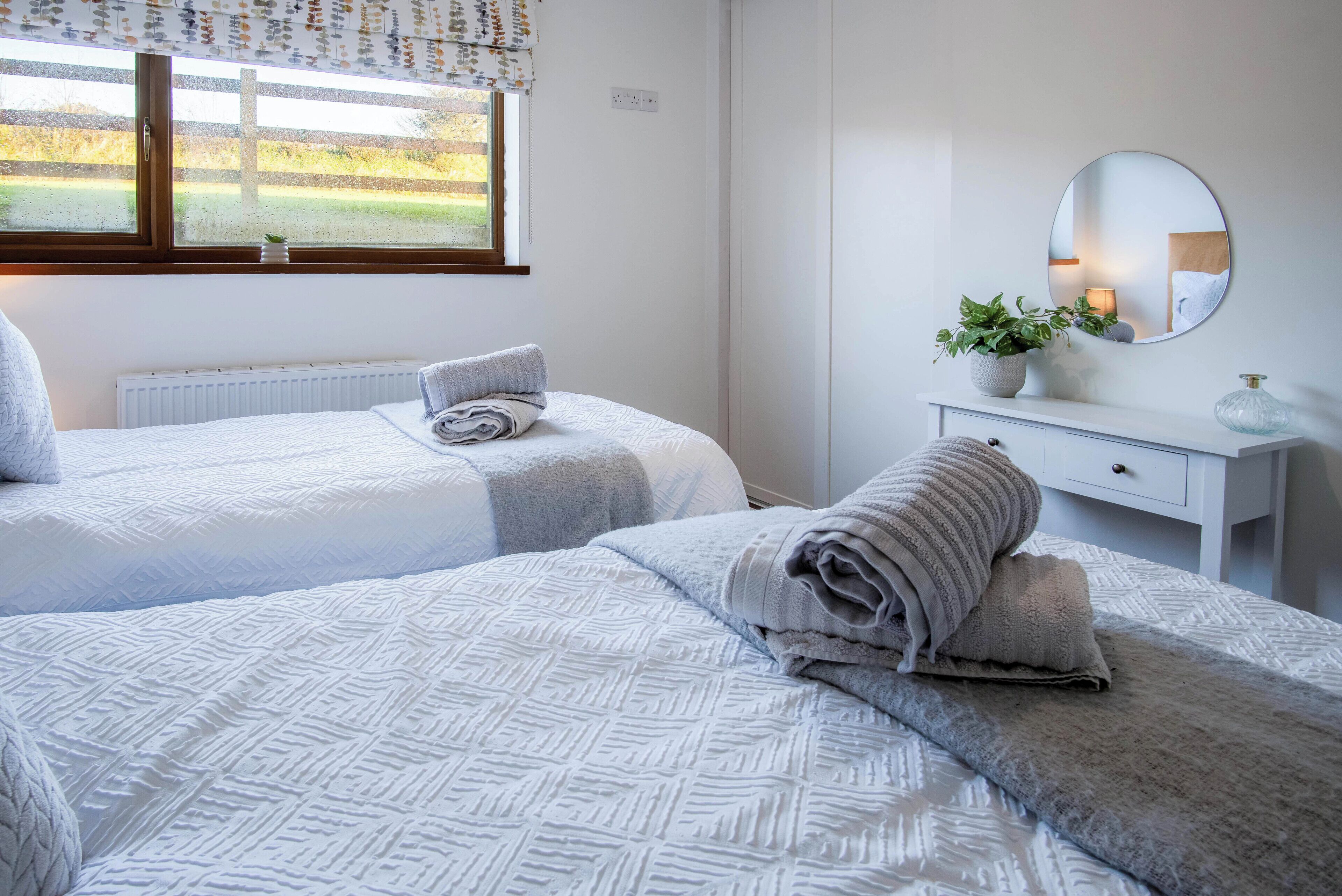 A bedroom with two beds, a dresser, a mirror, and a window with a view of a fence.