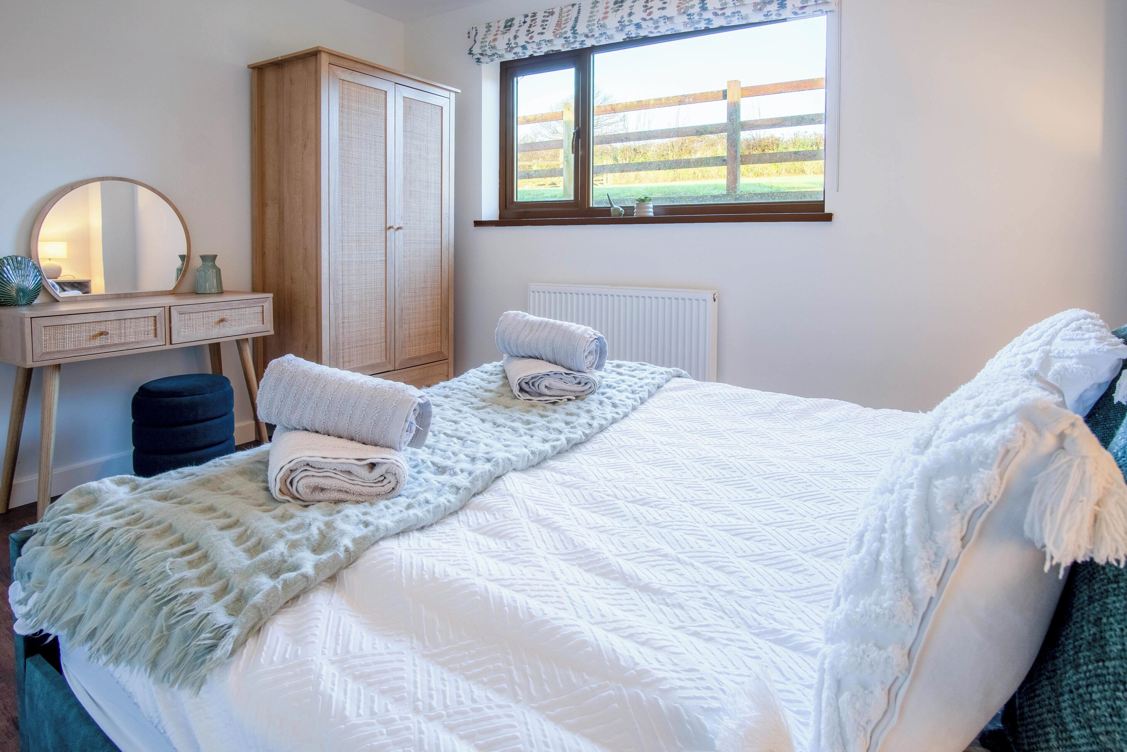 A bedroom with a bed, a dresser with a mirror, a window with a view of the outdoors, and a radiator.