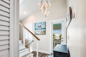 A staircase with a wooden handrail, a white door with a glass panel, and a painting of a lighthouse on the wall.