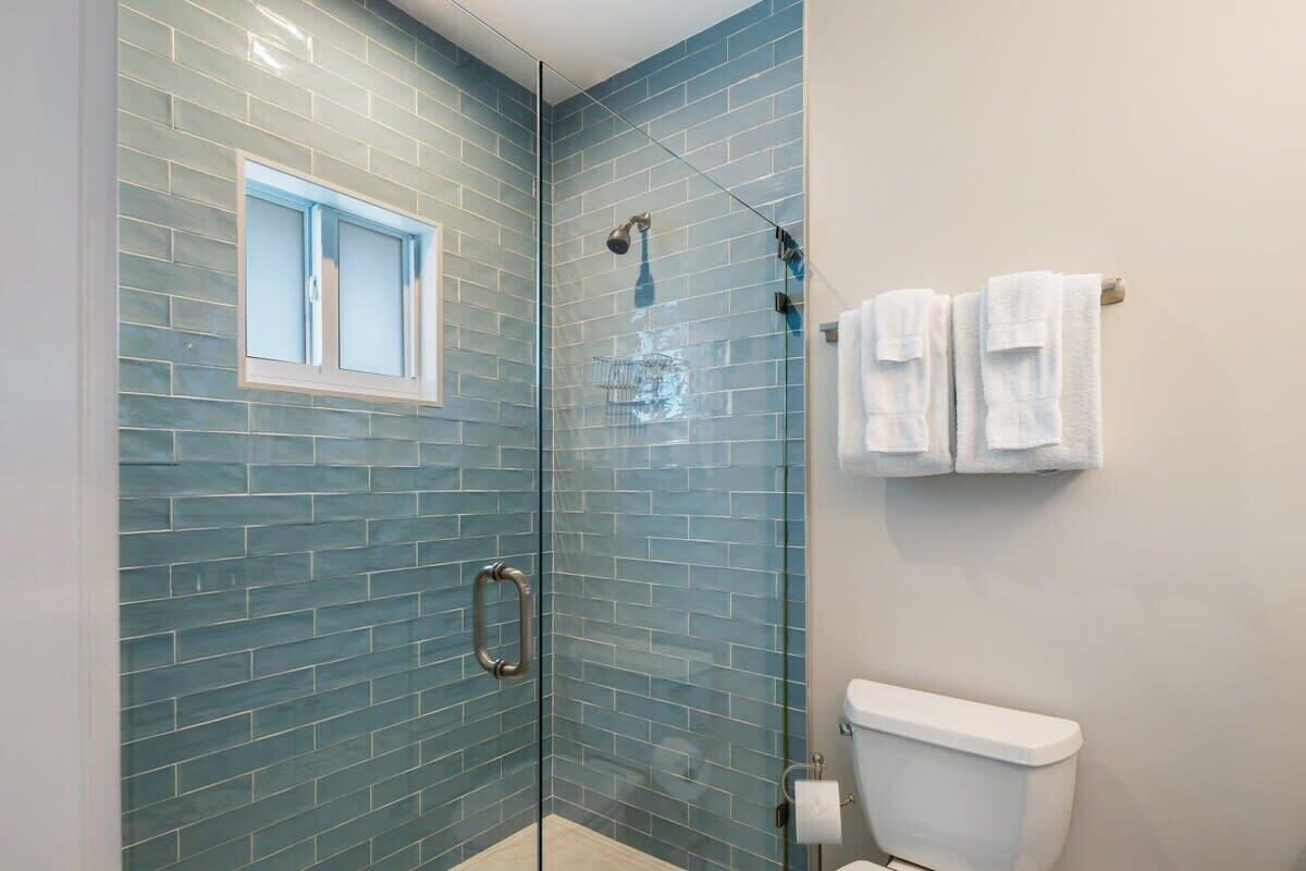 A bathroom with a glass shower enclosure, a toilet, and a window.