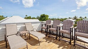 Une terrasse dotée de chaises longues et de fauteuils Adirondack, offrant une vue sur un quartier résidentiel avec ses maisons et sa verdure.