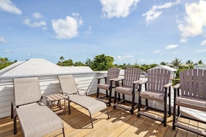 Une terrasse dotée de chaises longues et de fauteuils Adirondack, offrant une vue sur un quartier résidentiel avec ses maisons et sa verdure.