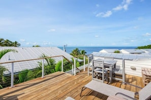Une terrasse en bois avec des sièges extérieurs, une vue dégagée sur l’océan et un paysage tropical.