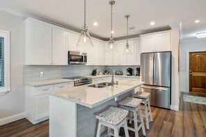 A modern kitchen with white cabinets, stainless steel appliances, a large island with bar stools, and pendant lighting.