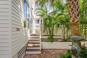 A narrow pathway leading to a white building with the number 1315, surrounded by lush greenery and a decorative bird sculpture. - Southernmost View - Private Pool (Key West)