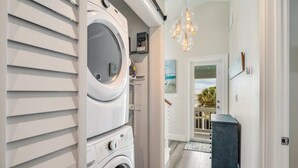 Une buanderie équipée d’un lave-linge et d’un sèche-linge à chargement frontal, d’une petite étagère avec quelques articles, et d’un couloir menant à une porte donnant sur l’extérieur.