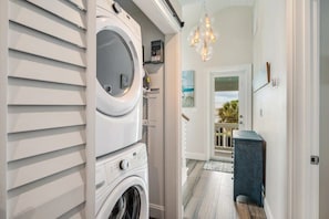 Une buanderie équipée d’un lave-linge et d’un sèche-linge à chargement frontal, d’une petite étagère avec quelques articles, et d’un couloir menant à une porte donnant sur l’extérieur.