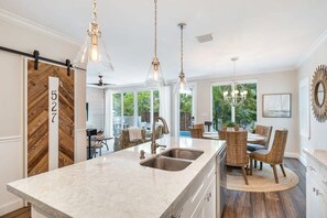 A kitchen with a large island, stainless steel sink, pendant lighting, and a dining area with wicker chairs. - Southernmost View - Private Pool (Key West)